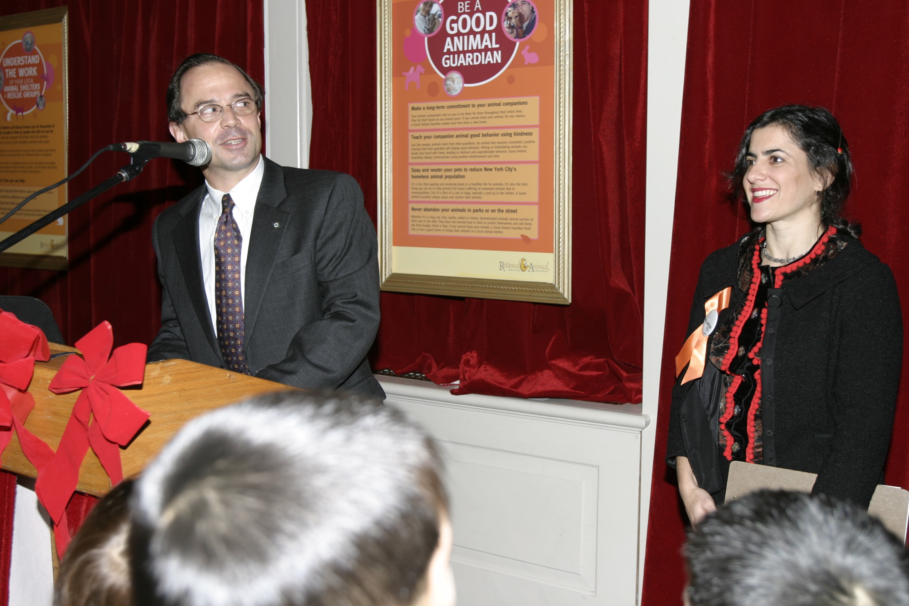 Two speakers at the opening ceremony podium with the Rational Animal Be a Good Animal Guardian poster behind them